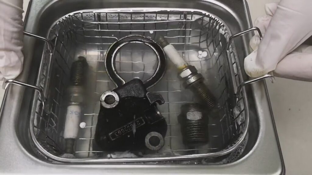 An operator using a stainless steel mesh basket to clean engine parts in an ultrasonic cleaner